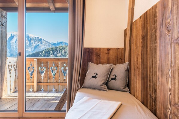 A bedroom with a wooden headboard, two pillows with deer designs, a bed with a white sheet, and a balcony with a view of mountains.