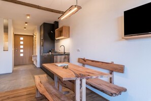 A modern kitchen with a wooden table and benches, a built-in oven, and a flat-screen TV mounted on the wall.