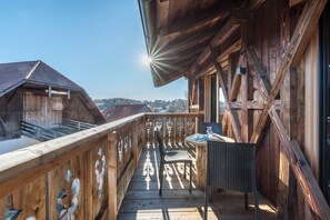 Un balcon en bois offrant une vue sur les bâtiments, avec une chaise et une table.