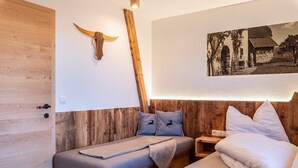 Een houten kamer met een bed, een nachtkastje, een houten hoorn bevestigd aan de muur, en een zwart-wit foto.