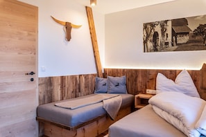 Une pièce en bois comprenant un lit, une table de chevet, un cornet en bois fixé au mur et une photographie en noir et blanc.
