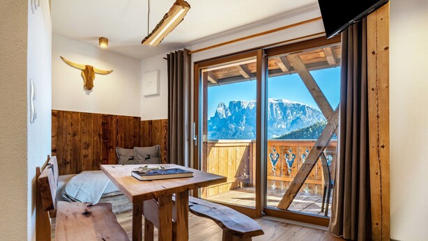 Een houten interieur met een tafel, een bank en een groot raam met uitzicht op de bergen.