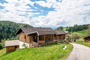 Ein Holzhaus mit Veranda, umgeben von einem Kiesweg und einer Wiese mit Wildblumen.