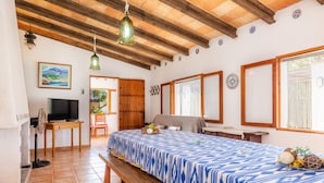 A room with a bed, wooden ceiling beams, a television, and a dining area.