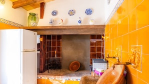 A kitchen with a white refrigerator, a hanging pot rack, a large ceramic sink, and a tiled backsplash.
