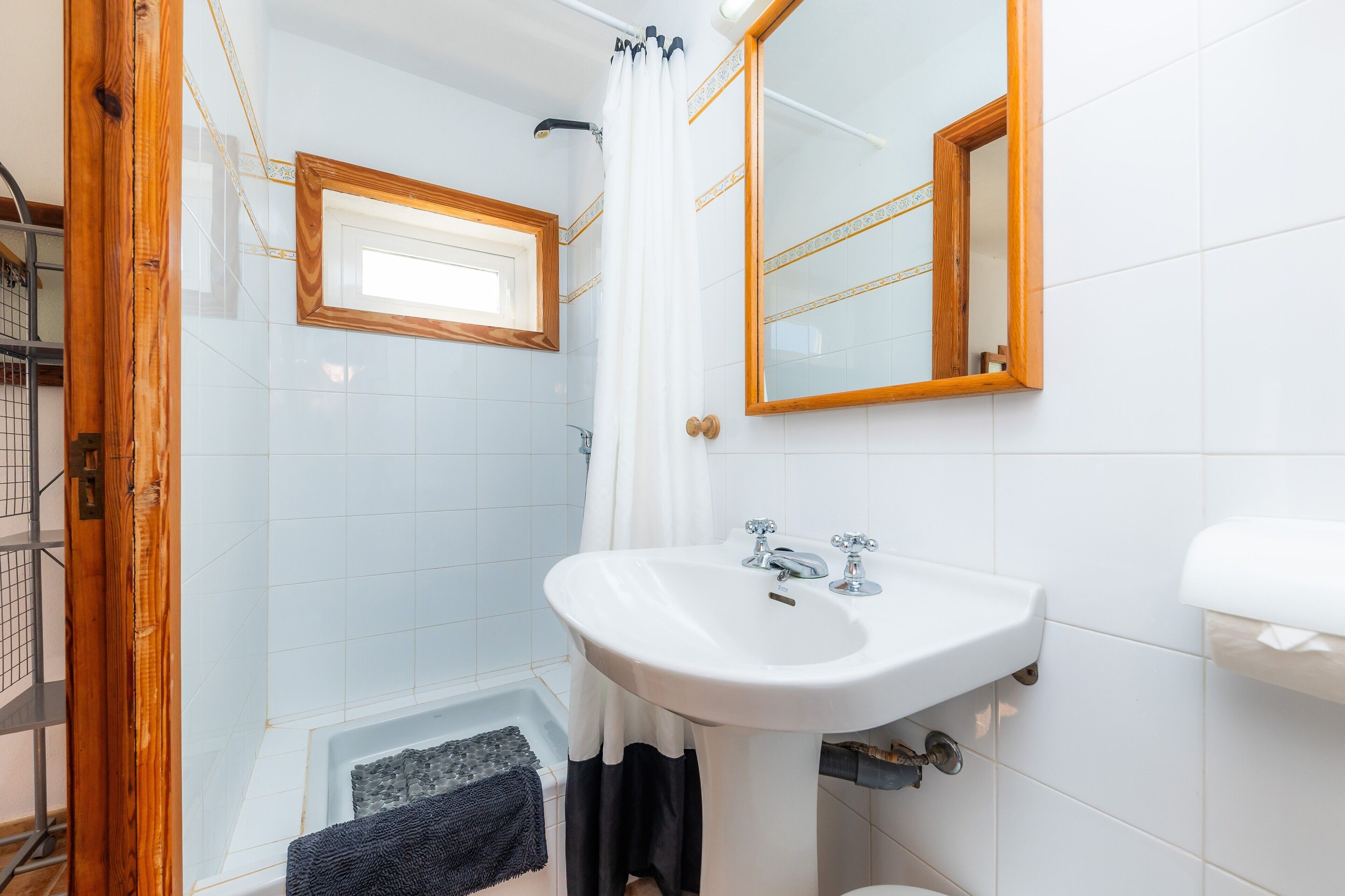 Une salle de bain avec un lavabo blanc, une douche avec un cadre en bois et un miroir avec un cadre en bois.