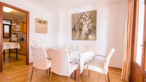 Un coin repas avec une table dressée pour six personnes, des chaises blanches et un tableau accroché au mur.