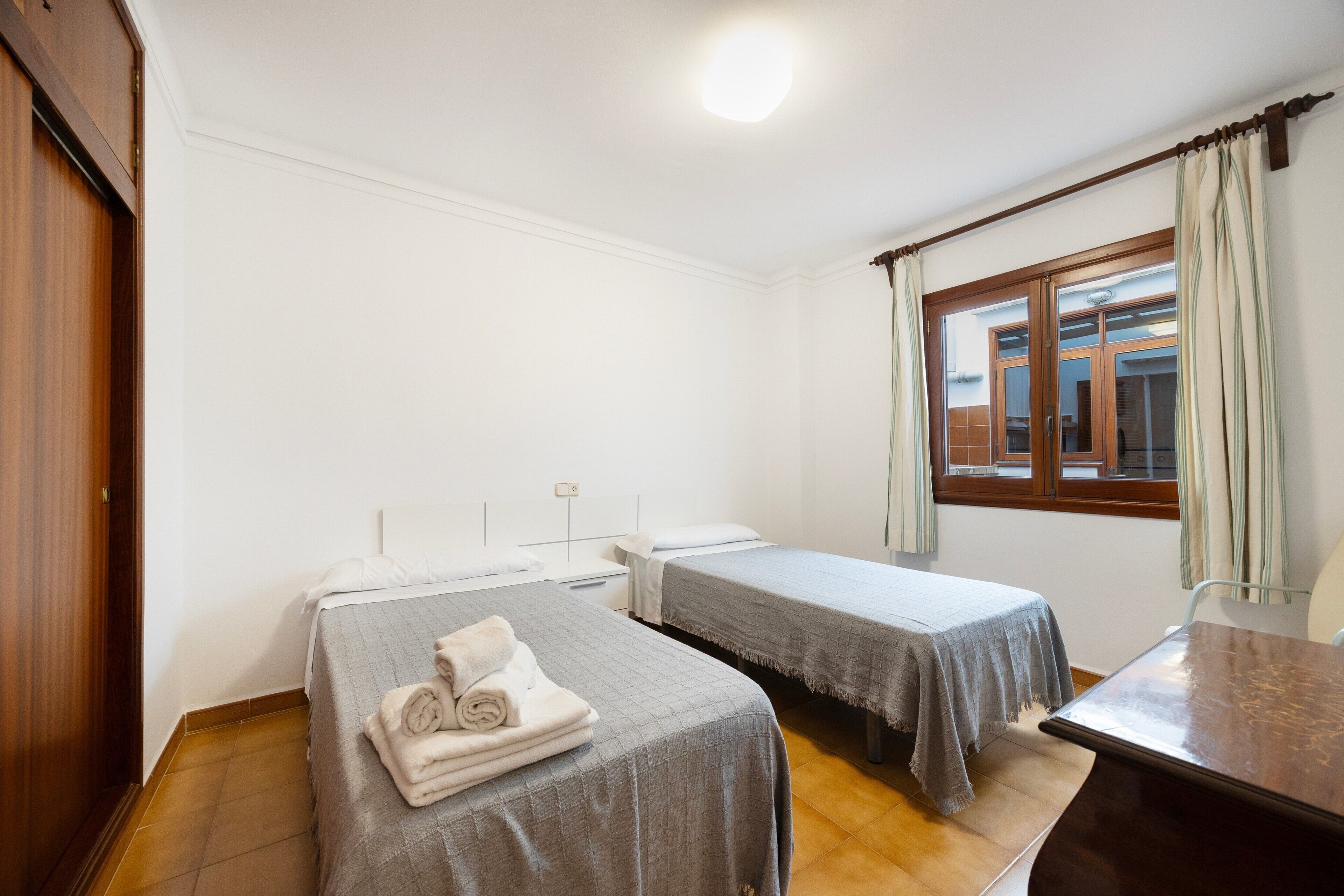 Ein Hotelzimmer mit zwei Einzelbetten, einem Holztisch, einem Fenster mit Vorhängen und einem Schrank aus Holz.