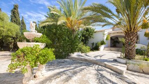 A garden with a fountain, palm trees, and a building entrance. - Country House 'Na Penyal Ref 246' with Sea View, Private Pool and Wi-Fi (Cala Millor)