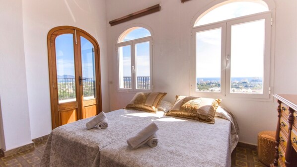 A bedroom with a bed, two windows, and a balcony.