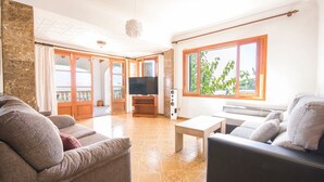 A spacious living room with a television, seating area, and large windows. - Country House 'Na Penyal Ref 246' with Sea View, Private Pool and Wi-Fi (Cala Millor)
