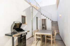 Una cocina compacta con una parrilla empotrada, un comedor con mesa y sillas, y una escalera que lleva a un nivel superior.