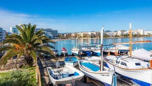 Un puerto deportivo con barcos amarrados, una palmera y edificios al fondo.