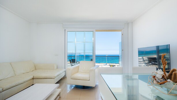 A modern living room with a sofa, armchair, and glass dining table, overlooking a balcony with a view of the sea. - Minimal Apartment Ref 9000 with Sea View, Balcony, Wi-Fi and Air Conditioning (Can Picafort)