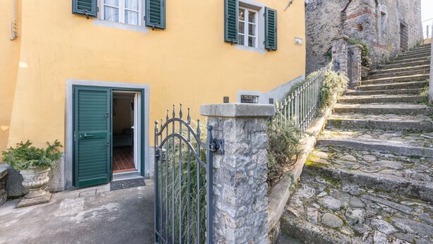 A yellow building with green shutters, a stone staircase, and a metal gate.