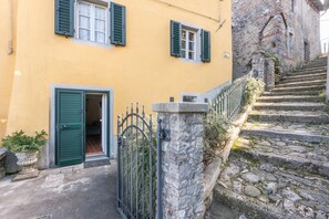 Un edificio amarillo con contraventanas verdes, una escalera de piedra y una verja de metal.
