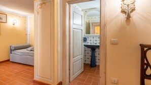A hallway with a sofa, a door, a wall-mounted light fixture, and a tiled floor.