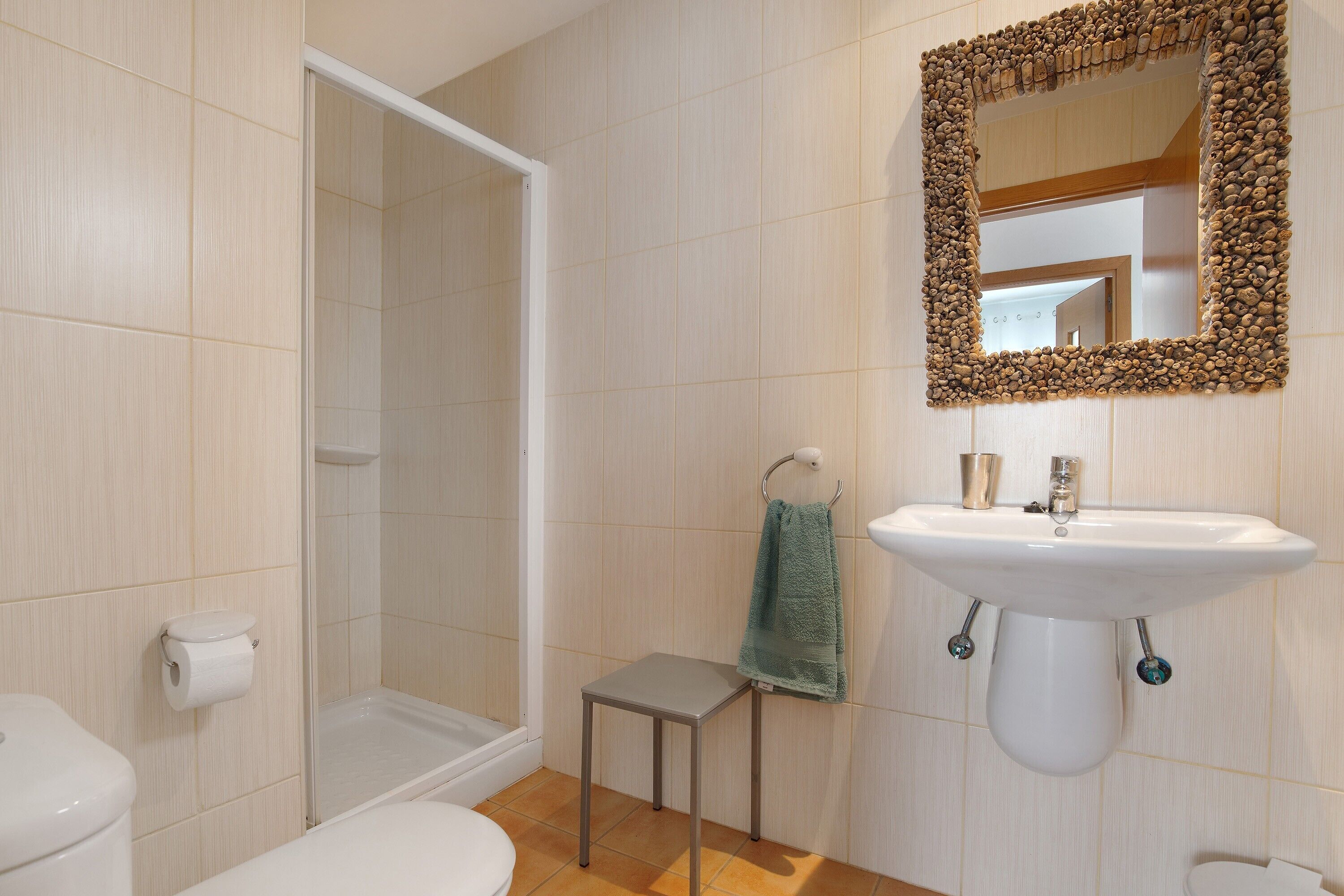 A bathroom with a shower, toilet, sink, and a mirror with a decorative frame.
