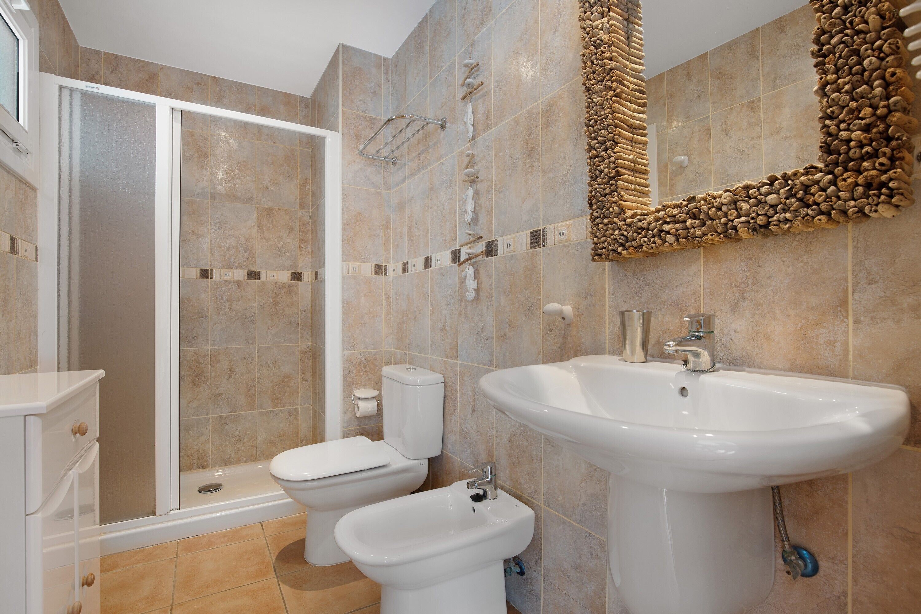 Un bany amb dutxa, vàter, bidet, rentapel i un mirall decoratiu.