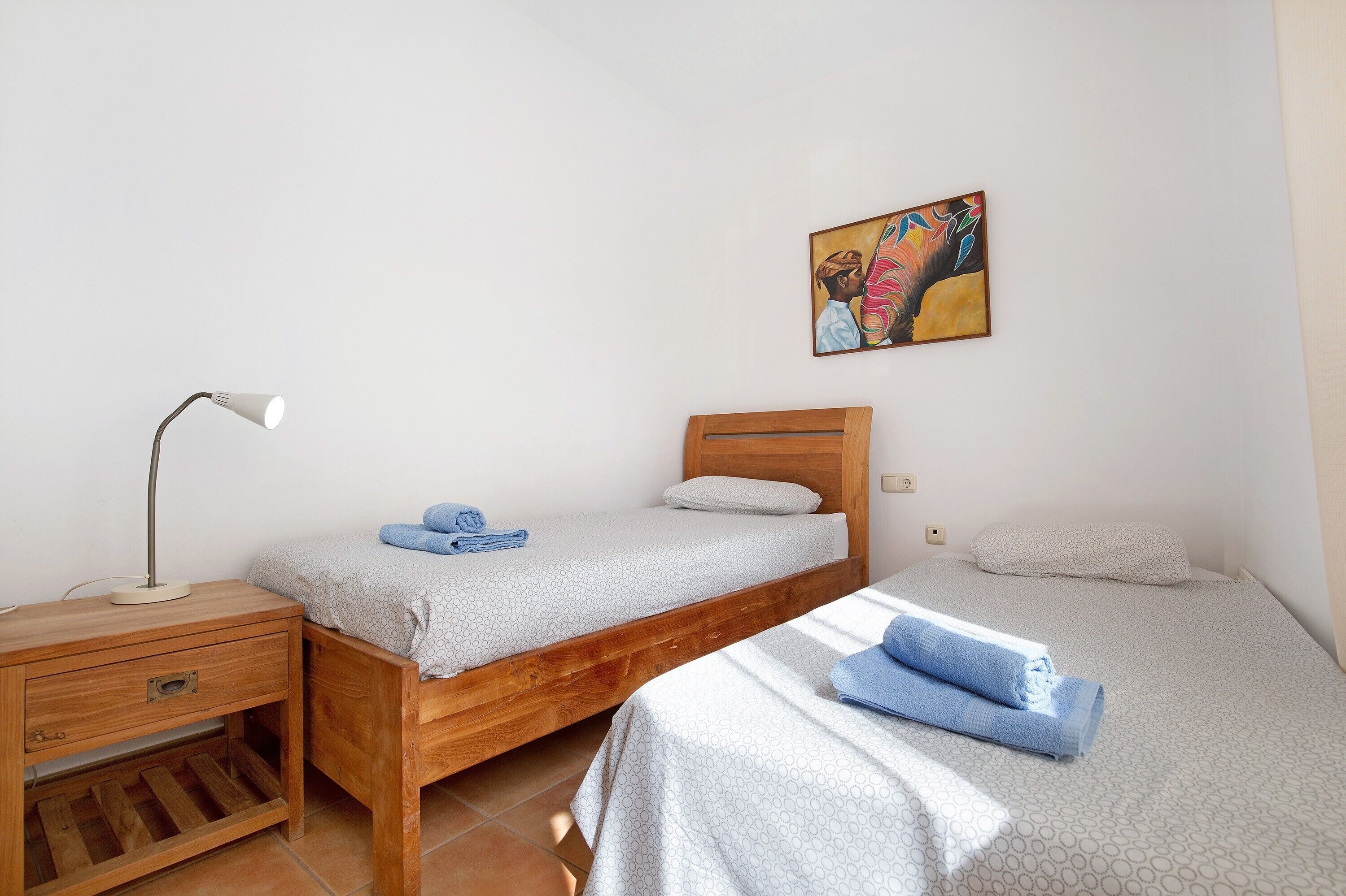 A room with two beds, a nightstand, a lamp, and a painting on the wall.