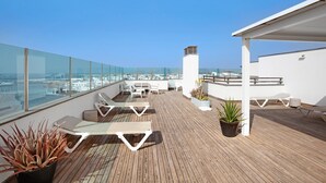 Une terrasse sur le toit, dotée de chaises longues, d’une plateforme en bois, de plantes en pot et offrant une vue sur le paysage urbain.