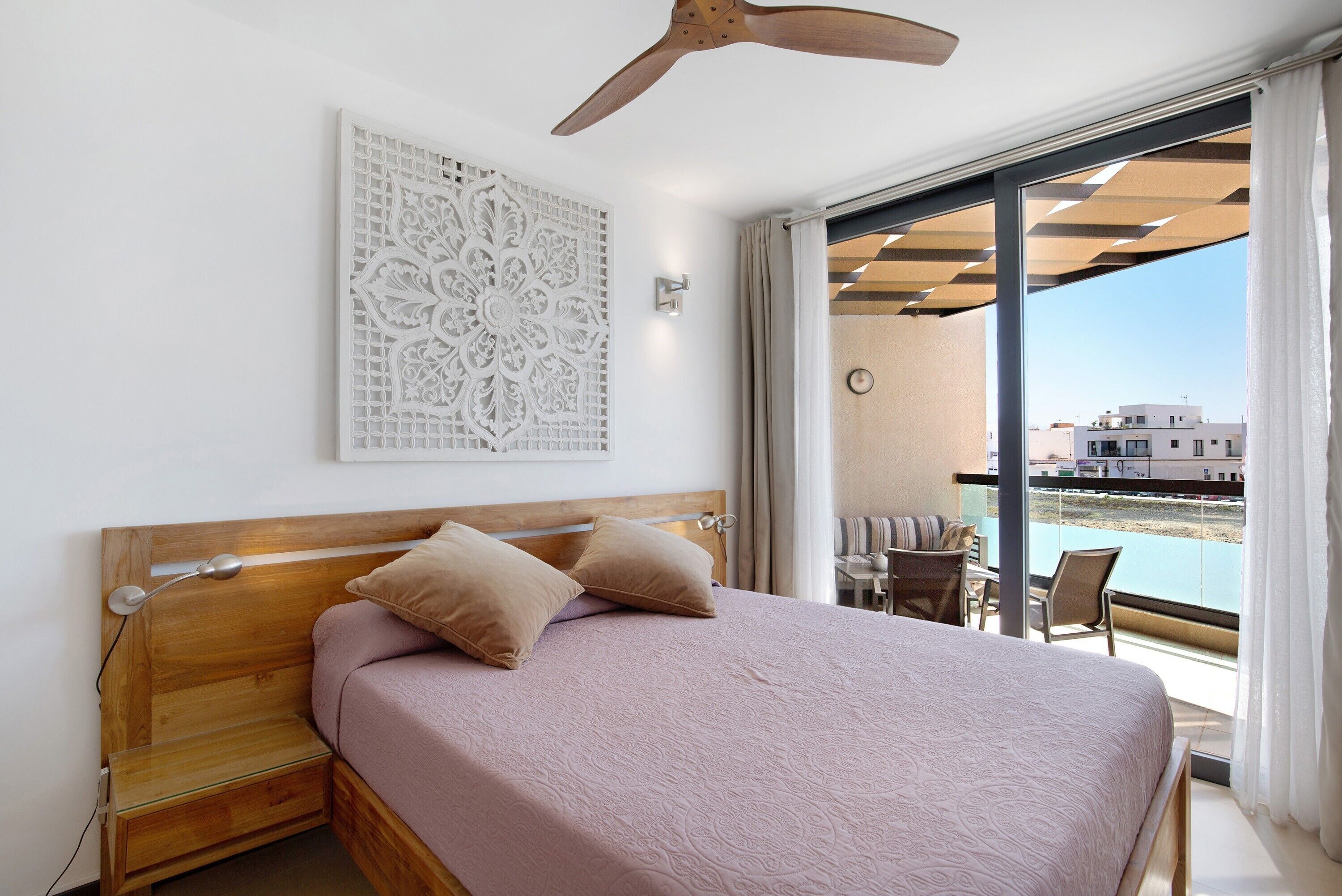 Un dormitorio con una cama, un ventilador de techo, una obra de arte en la pared y vistas al exterior.