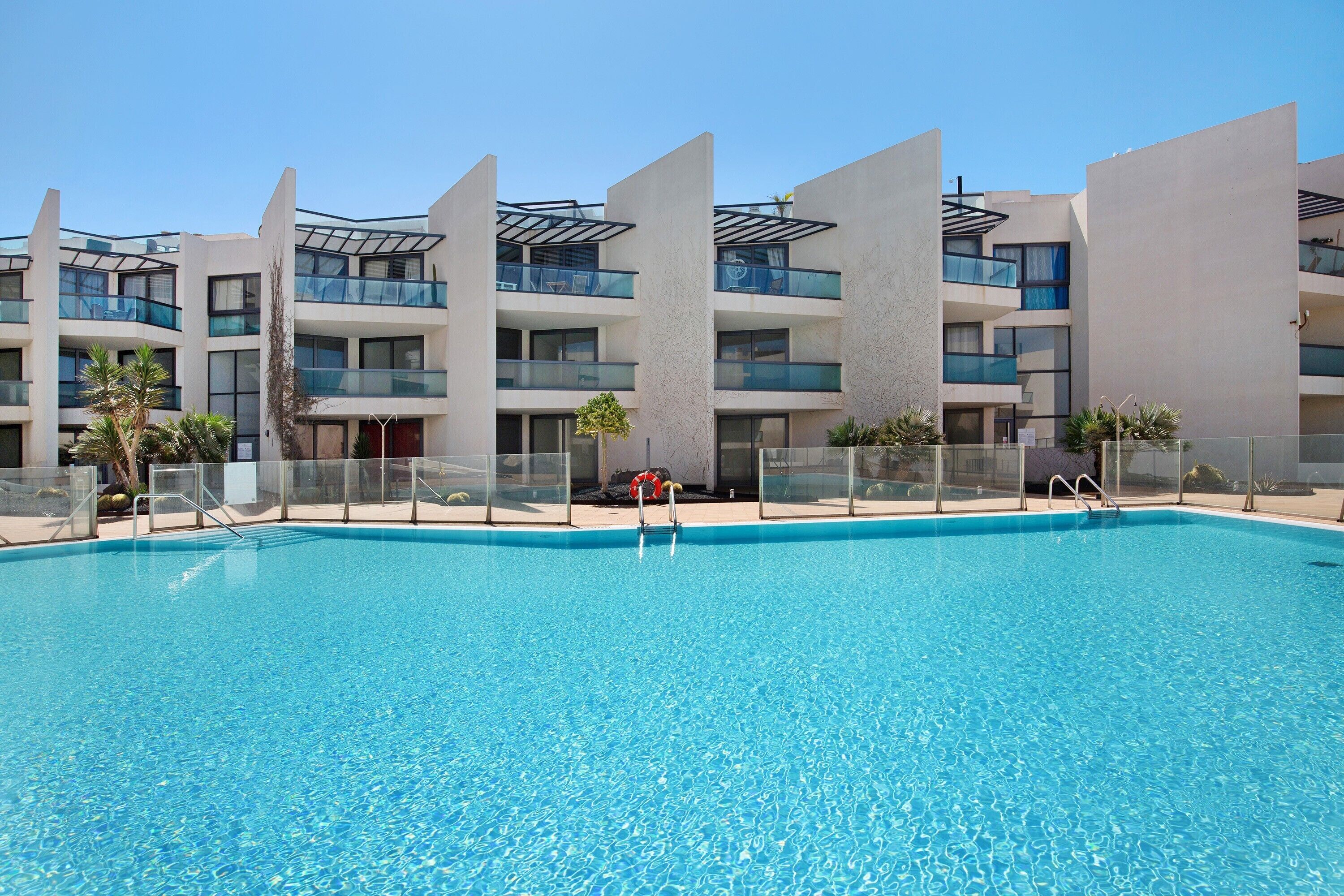 Et moderne hotel med swimmingpool, flere balkoner og en klar himmel.