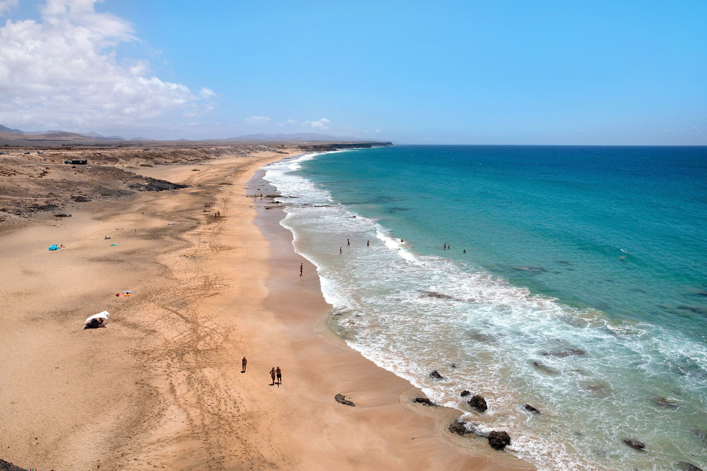 Una playa con agua azul cristalina, una orilla arenosa y montañas a lo lejos.