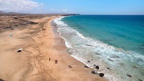Una playa con agua azul cristalina, una orilla arenosa y montañas a lo lejos.