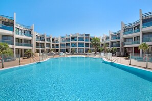 A modern hotel with a central swimming pool, multiple balconies, and a clear blue sky. - Holiday Apartment "Nautilus Sea View" near Beach with Pool & Wi-Fi (El Cotillo)