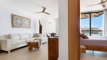 Una sala moderna con un sofá, una mesa de centro y un mueble de madera. Hay un ventilador de techo y una cama con vistas al exterior.