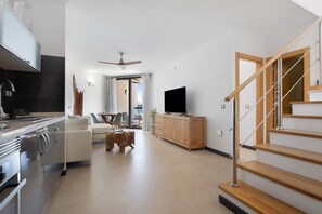 Moderni olohuone, jossa on keittiö, puinen portaikko ja litteänäyttöinen televisio.