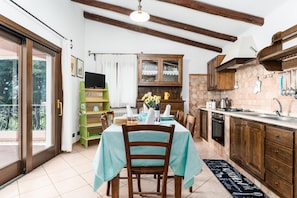 Une cuisine avec des meubles de rangement en bois, une table à manger avec des chaises, un four encastré et une fenêtre avec des rideaux.
