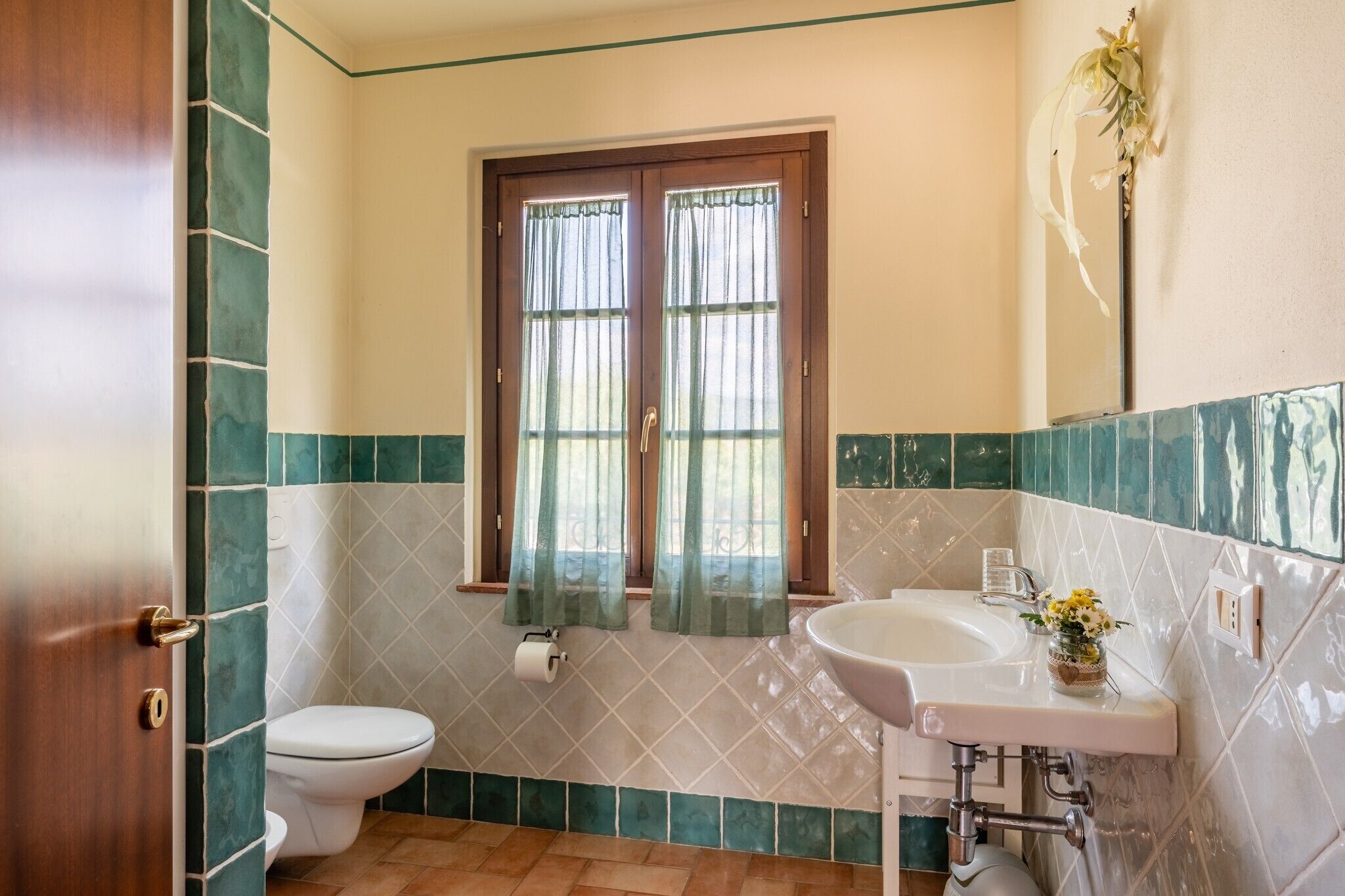 A bathroom with a toilet, sink, and window with curtains.