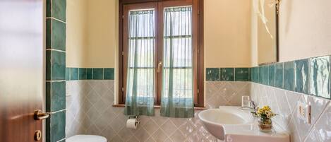 A bathroom with a toilet, sink, and window with curtains.