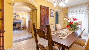 Un coin repas avec une table en bois, des chaises, un vase de fleurs et une cheminée en arrière-plan.