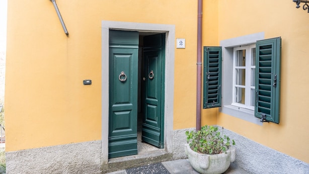 Un bâtiment à la façade jaune, avec une porte verte et une fenêtre dotée de volets verts.
