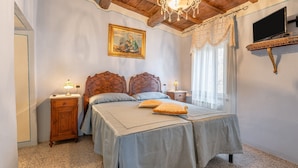 Une chambre avec un plafond en bois, un lit avec une tête de lit, une table de chevet, une lampe, un tableau, un téléviseur et une fenêtre avec des rideaux.