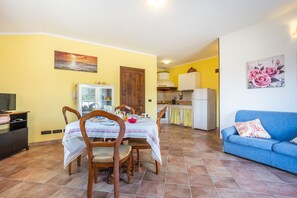A dining area with a table and chairs, a kitchen in the background, and a blue sofa with a floral cushion.