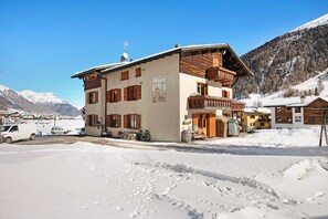 Ein mehrstöckiges Gebäude mit Balkon, einem Schild mit Bergmotiv und einer verschneiten Landschaft mit Bergen im Hintergrund.