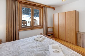 Ein Zimmer mit einem Bett, einem Holzschrank, einem Fenster mit Vorhängen und Blick auf eine verschneite Landschaft.