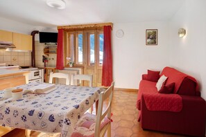 Ein gemütliches Zimmer mit Esstisch, einem roten Sofa, einem Fenster mit Vorhängen, einer Uhr und einer Wandleuchte.