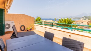 A terrace with a table and chairs, a green railing, and a view of the sea and buildings.