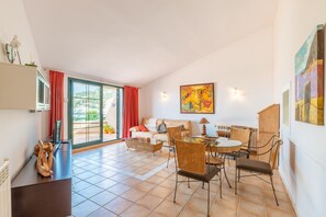 Un vaste espace de vie comprenant un canapé, une table à manger et des chaises, une grande fenêtre avec des rideaux et un tableau accroché au mur.