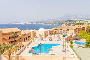 Un complexe hôtelier doté d’une piscine, de chaises longues, de parasols et offrant une vue sur la mer et les montagnes.