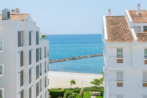Um edifício costeiro com vista para o mar, um molhe rochoso e uma praia arenosa.
