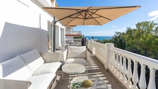 A balcony with white furniture, a table with a pineapple, and a large umbrella. - Holiday Home 'Modern Villa with Private Pool' with Sea View, Wi-Fi and Air Conditioning (MIJAS)