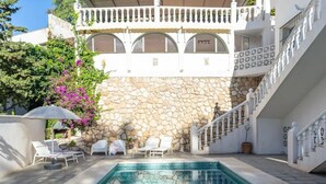 A pool area with lounge chairs, a stone wall, and a staircase leading to a balcony. - Holiday Home 'Modern Villa with Private Pool' with Sea View, Wi-Fi and Air Conditioning (MIJAS)