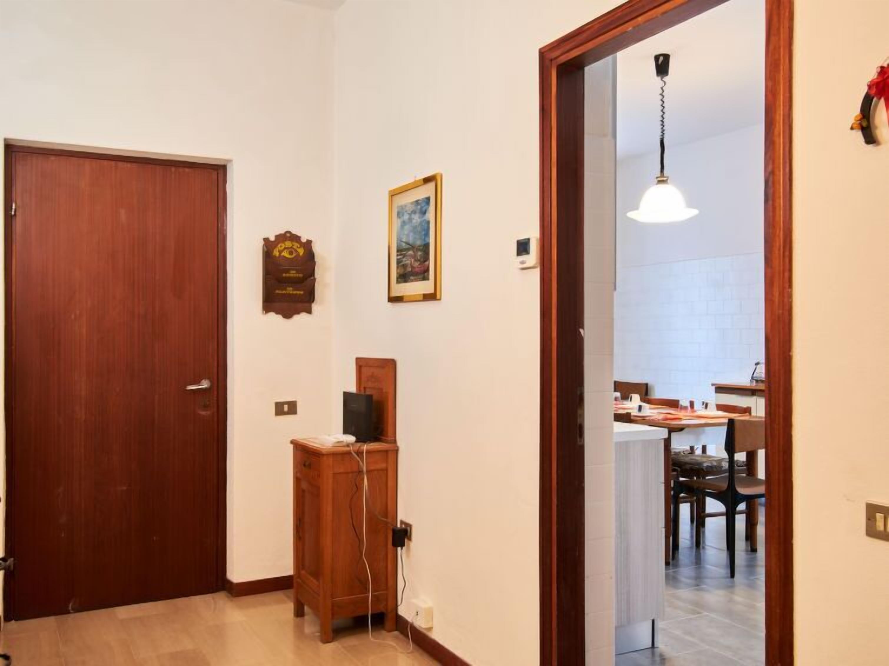 Un couloir avec une porte en bois, un tableau encadré, un petit meuble et un coin repas comprenant des chaises et une table.