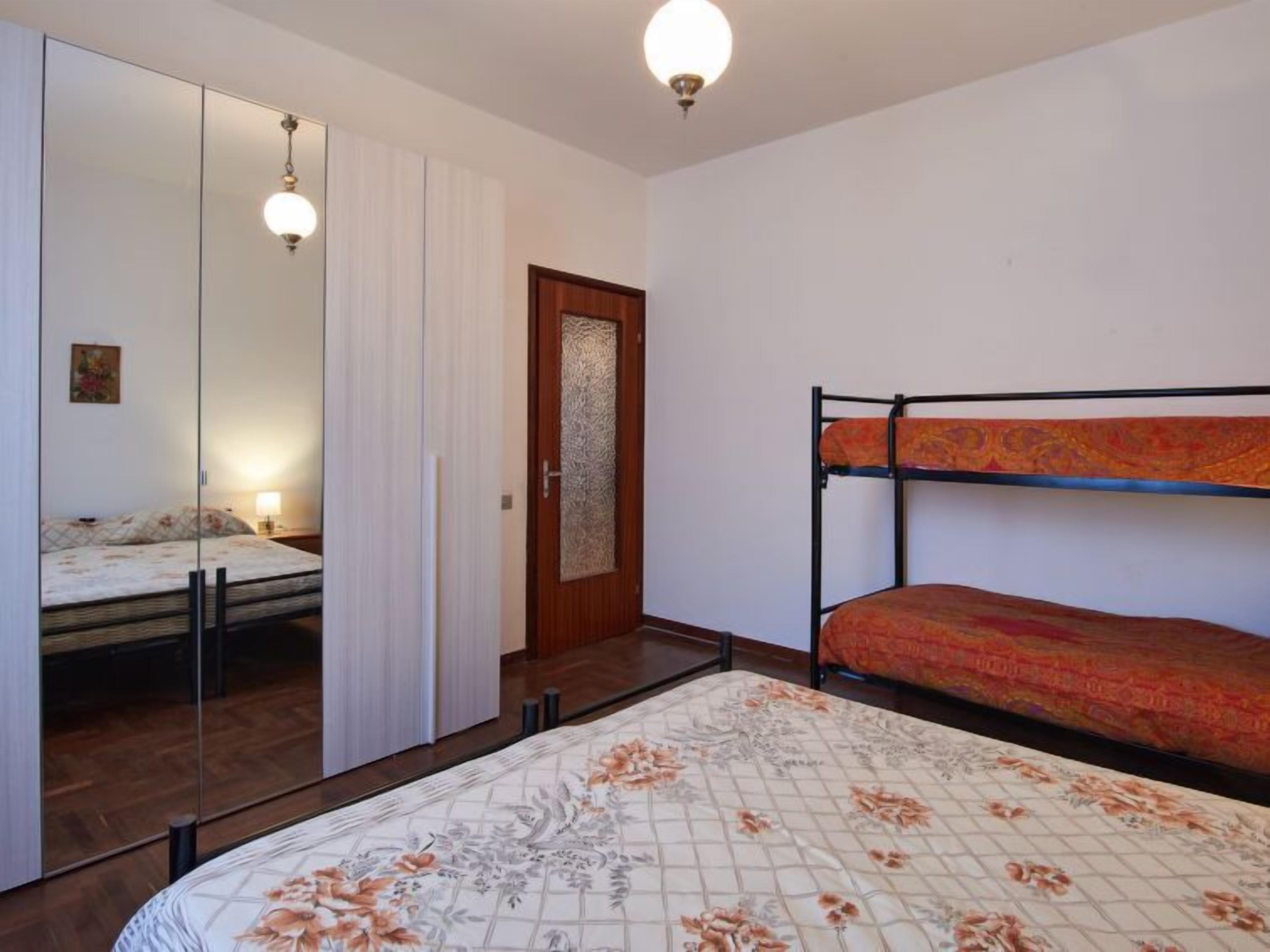 A bedroom with a bunk bed, a large mirror, and a wooden door with a decorative panel.